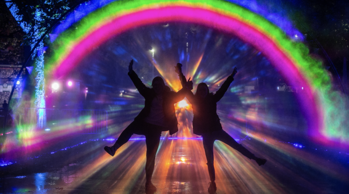 People with their arms up in front of a rainbow of light