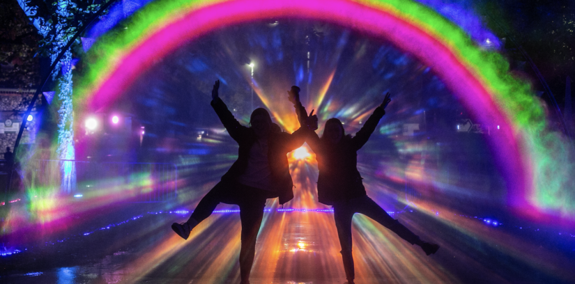 People with their arms up in front of a rainbow of light