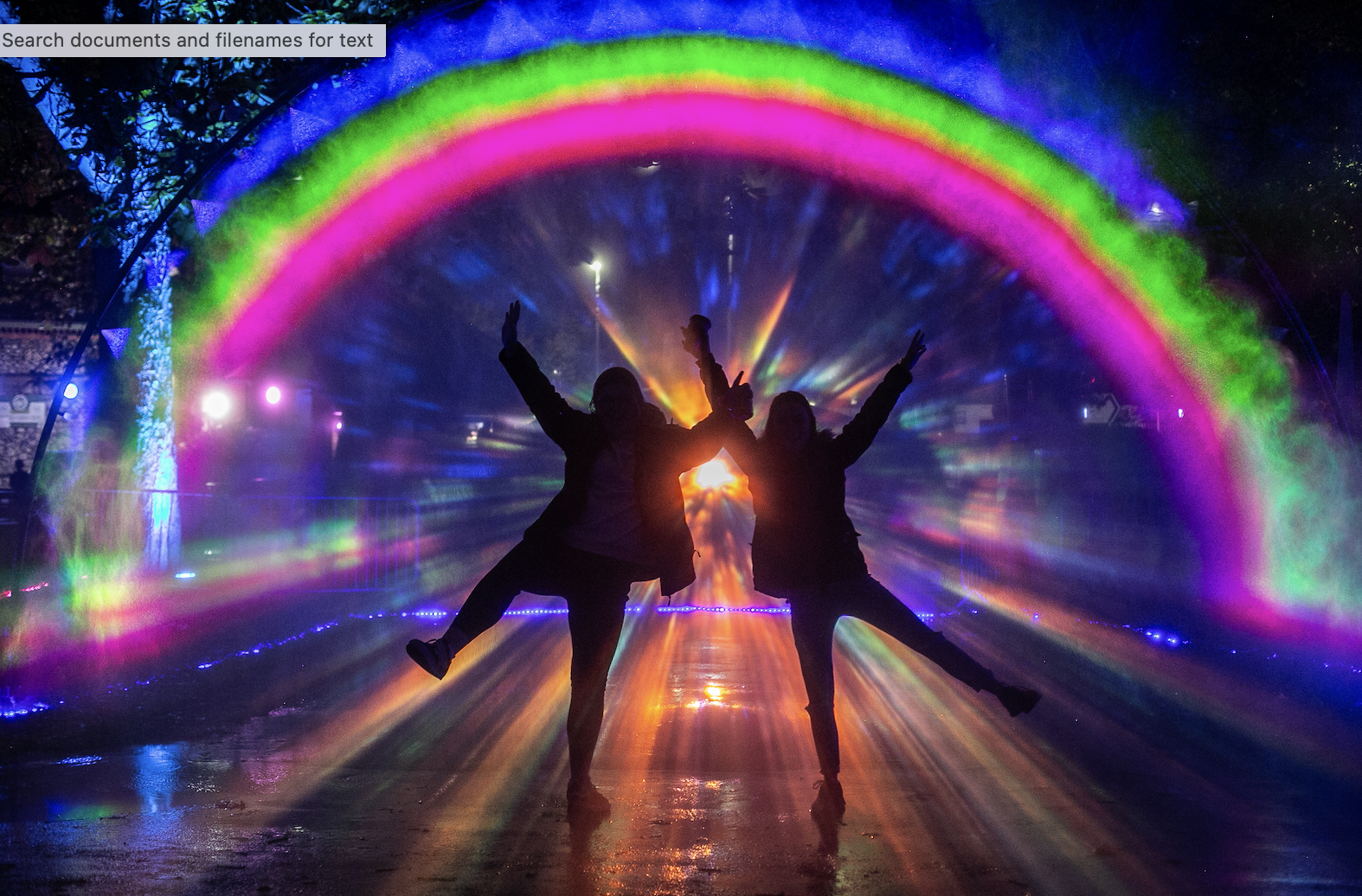 People with their arms up in front of a rainbow of light